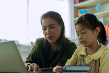 Obraz premium A Beautiful Asian mother busy working while looking after and teaching her children on a laptop computer at home