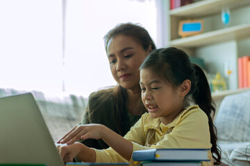 A Beautiful Asian mother busy working while looking after and teaching her children on a laptop computer at home