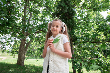 little girl with tails in green forest. The child smiles and holds a leaf