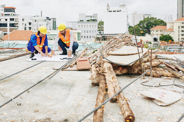 Construction workers checking blueprint on the ground next to pile of rebar and lumber before starting work