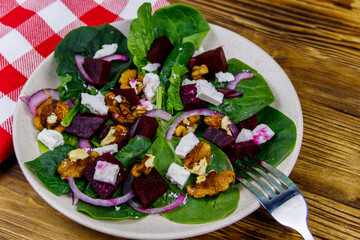 Tasty spinach salad with boiled beetroot, feta cheese, walnut and red onion on wooden table. Healthy vegetarian food