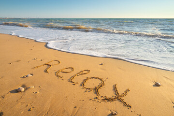 Word Relax handwritten on sandy beach at sunset.