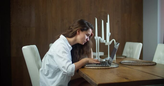 A young brunette woman sits at home at a table and works on a laptop. Fatigue, pain in the head, but you need to continue to work