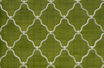 Fototapeta premium Pattern of diamond shape on white curved wrought iron steel on the lattice window, green bamboo curtain background, lattice work for house decoration