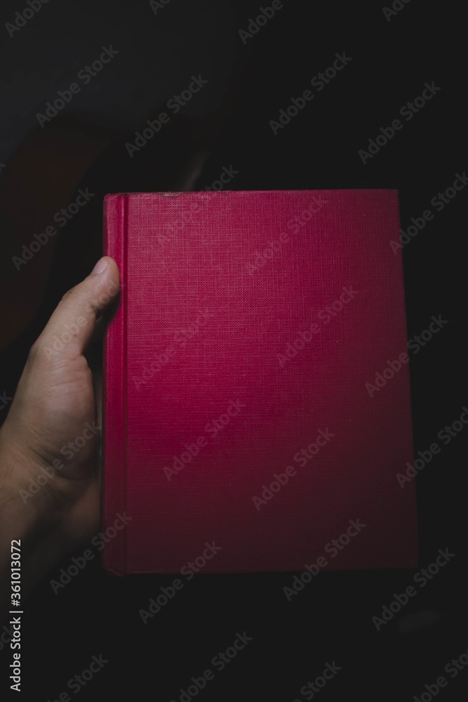 Poster Vertical shot of a person holding a book with a red cover isolated on a dark background