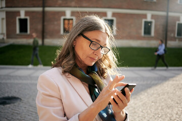 Summer portrait of busy beautiful middle aged gray haired European female in stylish eyewear...