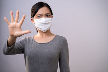 Don't Touch Your Face. Asian woman wearing protective face mask showing hand making stop sign standing isolated on background.