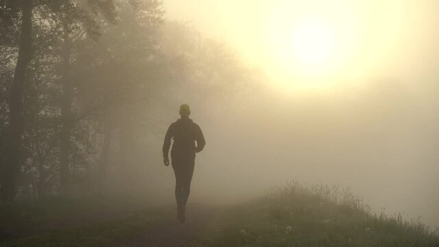 Athlete running on a gravel road during a foggy, spring sunrise in the countryside.