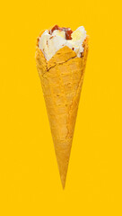 side view vanilla flaovr ice cream cone with couple of bites on a yellow background