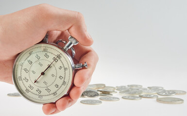 time is money. hand holding a stopwatch on a background of silver coins