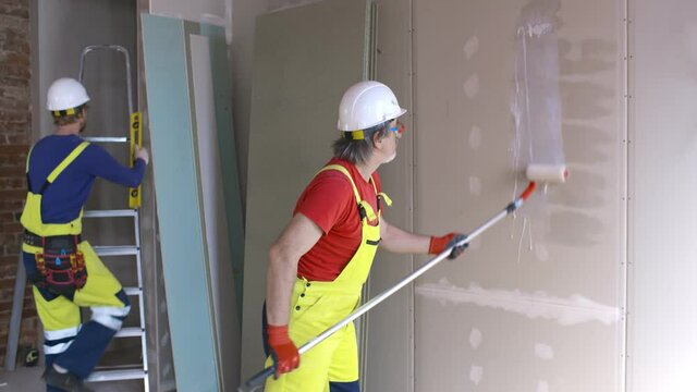 Worker applying primer to wall with long roller on construction site