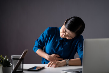 Asian woman in blue shirt was sick with stomach ache sitting at office. isolated on white background.