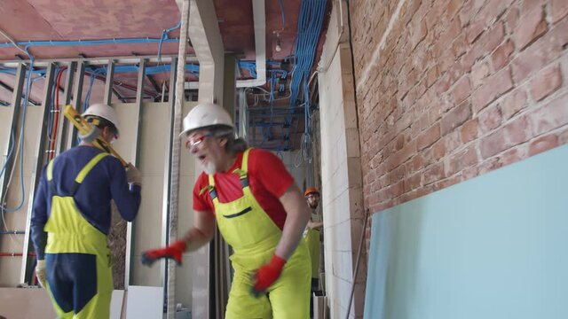 Mature workman in helmet enjoy dancing while listening to music at construction site