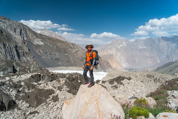 Young Asian man trekker standing on rock in Patundas trekking route in Karakoram mountains range, Hunza valley, North Pakistan