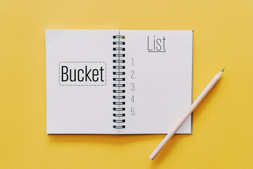 Notebook and pencil with bucket list words on pastel color background.