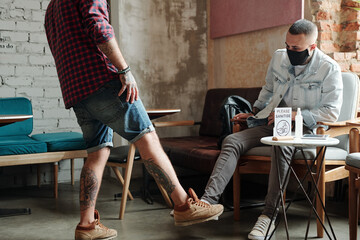 Young men greeting each other with foot gesture while meeting in cafe after coronavirus quarantine