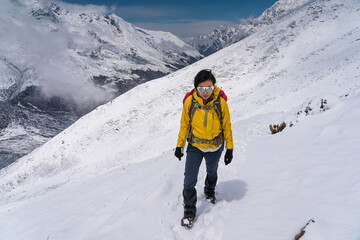 Fototapeta na wymiar Young Asian woman trekking in Langtang valley after heavy snow storm. A woman trekking on trail that covered by fresh snow. Himalaya mountains range, Nepal