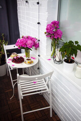 Bouquet of peony flowers, two cups of tea and fresh cherries on white table. Modern balcony interior.