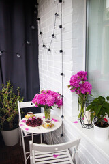 Bouquet of peony flowers, two cups of tea and fresh cherries on white table. Modern balcony interior.
