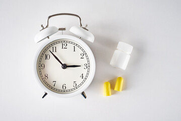 Insomnia problem concept. Alarm clock, ear plugs and pills on a white background