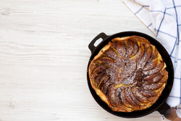 Homemade Apple Dutch Pannekoek Pancake in a cast-iron pan on a white wooden surface, top view. Overhead, from above, flat lay. Space for text.