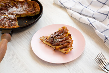 Homemade Apple Dutch Pannekoek Pancake on a pink plate on a white wooden background, side view.