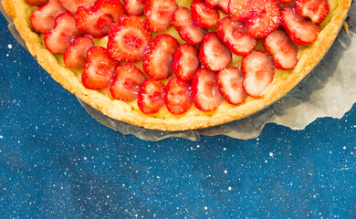 Fresh homemade strawberry shortcrust tart pie stuffed with custard vanilla cream . Sliced berries and mint leaf on the trendy phantom blue cosmos background. Free copy space. Top view.