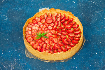 Fresh homemade strawberry shortcrust tart pie stuffed with custard vanilla cream . Sliced berries and mint leaf on the trendy phantom blue cosmos background. Free copy space. Top view.