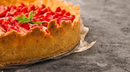 Fresh homemade strawberry shortcrust tart pie stuffed with custard vanilla cream . Sliced berries and mint leaf on the trendy dark grey concrete background. Free copy space. Top view.
