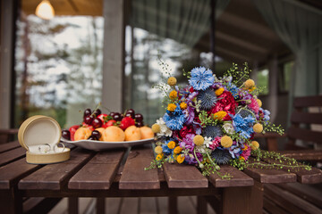 Wedding rings, juicy fruits, a wedding bouquet. Beautiful details on the set in the country