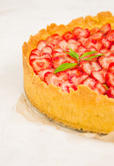 Fresh homemade strawberry shortcrust tart pie stuffed with custard vanilla cream . Sliced berries and mint leaf on the trendy white concrete background isolated. Free copy space. Top view.