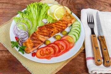 Serving of grilled trout fillet among vegetables on rustic table