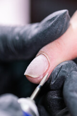 Close-up shot of hardware manicure in a beauty salon. Manicurist is applying electric nail file drill to manicure on female fingers.