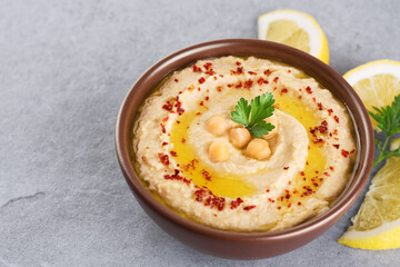 Chickpeas hummus with olive oil, paprika, parsley and lemon on a gray background.