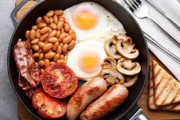 English breakfast in a pan on a gray background. Fried sausages, bacon, eggs, mushrooms, tomatoes and beans.