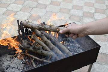 A man fires a barbecue grill, tossing fruit wood into the fire.