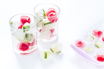 Cocktail glasses with berries in ice cubes on white table