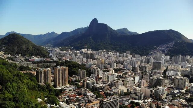 FORWARD MOVING DRONE OVER BUILDINGS IN RIO DE JANEIRO IN A SUNNY DAY WITH THE STATUE OF CHRIST THE REDEEMER CENTERED
