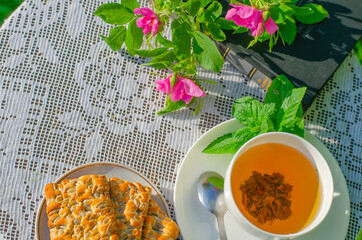 A Cup of green tea with a mint leaf, flowers, and a book on a table in the garden. Evening tea with cookies. Summer village concept. Copy space.