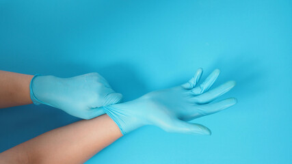 The hand is pulling doctor gloves or blue latex gloves of the right hand on a blue background.