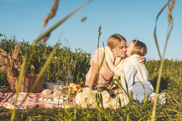 Happy mother and daughter have a rest together in a picnic outdoors. Blue pink clothes, casual.