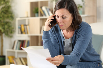 Adult woman calling on phone checking letter at home