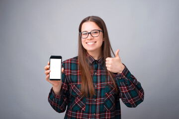 Photo of cheerful young woman showing thumbs up and smartphone screen.