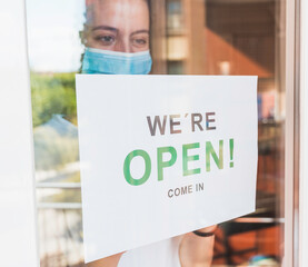 Business owner with a face mask hanging the open sign in her restaurant. Woman with a face mask...