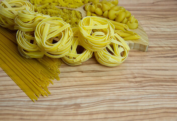 Pasta nests spaghetti scallops linguini penne tagliatelle fusilli spirals on a blackboard and wooden background.