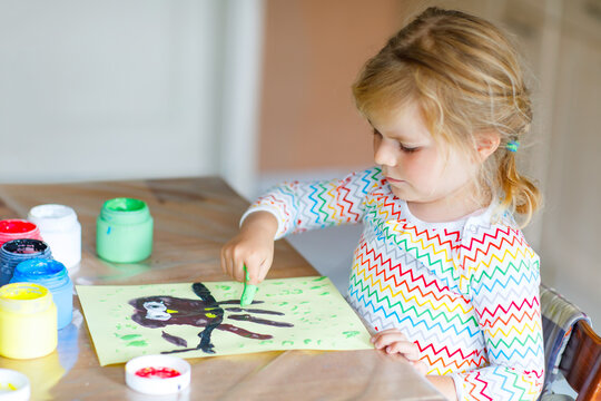 Little creative toddler girl painting with finger colors an owl bird. Active child having fun with drawing at home, in kindergaten or preschool. Games, education and distance learning for kids