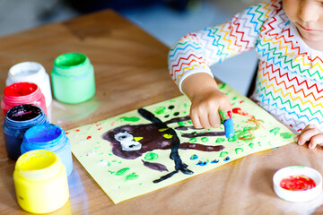 Closeup of little creative toddler girl painting with finger colors an owl bird. Child having fun with drawing at home, in kindergaten or preschool. Games, education and distance learning for kids.