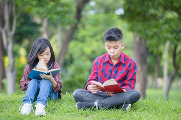 Brother and sister sitting on the grass and reading the book in the park, Kids playing & Outdoor learning concept