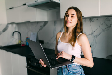 Happy young woman using laptop in kitchen