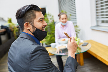 Business Mann mit Mundschutz am Kinn beim Snack essen